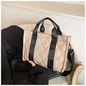 Dettaglio della borsa tote trapuntata beige con tracolla nera sulla sedia