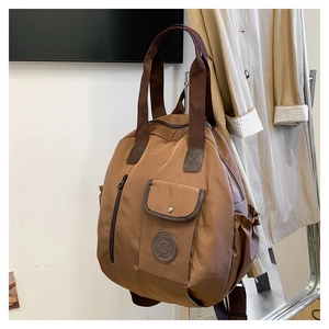 Detail of a brown waterproof nylon backpack featuring a logo patch and magnetic flap pocket