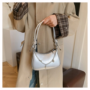 Detail of silver crescent bag featuring chic chain charms and knotted strap accents