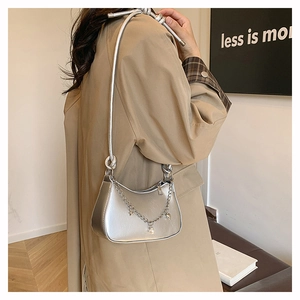 Silver crescent underarm bag with metal chains and star charms shown on beige coat