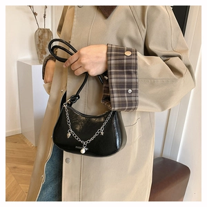 Detail of black crescent bag with glossy finish and decorative silver charm chain