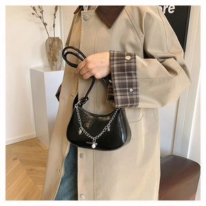 Detail of black patent leather crescent bag with silver chain and pearl charms on a model