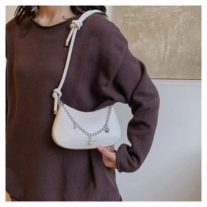 Close-up of white crescent bag with silver chain and pearl pendant on a model