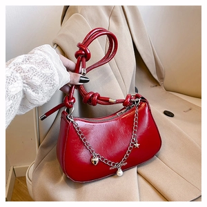 Detail of red crescent shoulder bag featuring gold chain and decorative heart charms