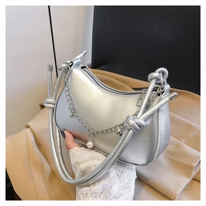 Detail of silver crescent bag featuring textured metallic finish and pearl heart chain
