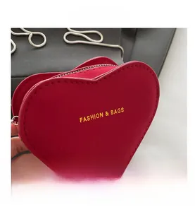 Detailed macro view of heart-shaped red suede bag with gold lettering and silver zipper