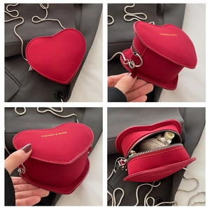 Detail view of red heart-shaped crossbody bag with gold text and metal chain strap