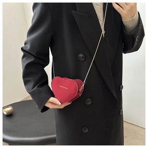 Detail shot of a red heart-shaped mini crossbody bag with silver chain on black blazer