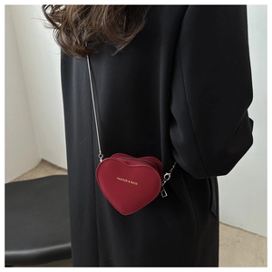Detail of red heart-shaped crossbody bag with gold lettering and silver chain strap