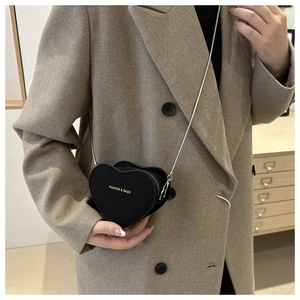 Close-up of heart-shaped black crossbody bag with gold fashion text and chain strap