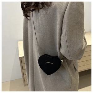 Side view of heart-shaped black leather bag with gold lettering and silver chain strap
