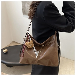 Detailed side view of brown faux leather tote with plush bear charm and adjustable straps