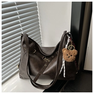 Macro shot of dark brown vintage faux leather tote with plush bear charm and metal buckle