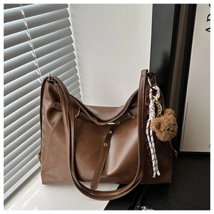 Brown leather Hobo tote bag with woven rope detail and plush bear charm by the window