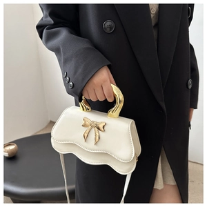 Detail of elegant cream leather handbag with golden metal bow clasp and wavy edge design