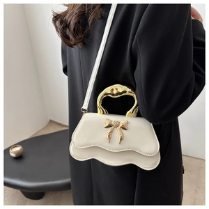 Detail of white leather handbag with golden metal bow and unique wavy bottom edge