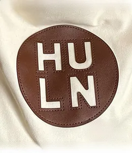 Close-up of brown leather HULN logo patch with cutout letters on a white tote bag