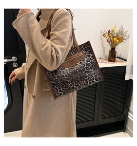 Side view of leopard print tote bag with brown leather trim and shoulder strap worn by model