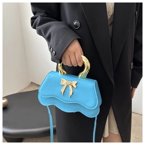 Detail of bright blue bag with golden butterfly buckle and metallic handle on black suit