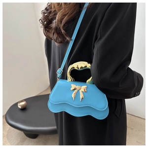 Detail of light blue wave-shaped handbag with golden bow decoration and metal handle