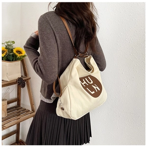 Detail of off-white canvas tote bag with brown straps and circular HU LN logo