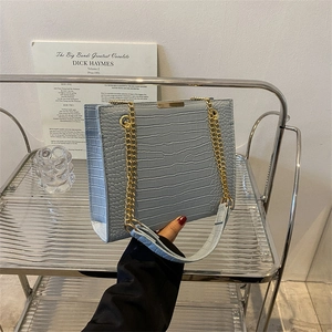 Blue crocodile pattern chain shoulder bag on metal display stand with artistic background