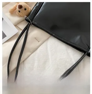Detail of black faux leather tote bag with thin straps and a brown plush bear charm