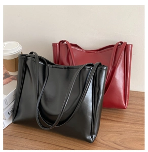 Minimalist faux leather tote bags in black and burgundy displayed on a wooden table
