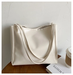 Minimalist cream white leather tote bag featuring sleek stitching and long handles