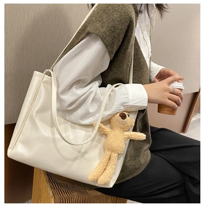 Detail of a large beige leather tote bag with a cute teddy bear charm hanging from the handle