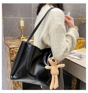 Large black glossy PU tote bag with a brown teddy bear charm worn by a model in a knit sweater