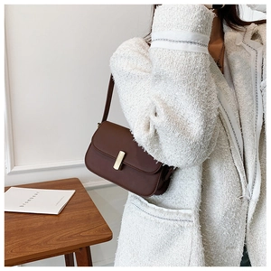 Side view of dark brown minimalist shoulder bag with gold metal clasp on a wooden table