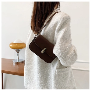 Detail of dark brown leather crossbody bag with metal clasp and slender shoulder strap