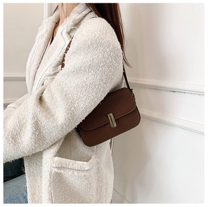 Detail of a brown leather crossbody bag with a gold metal buckle on a tweed jacket