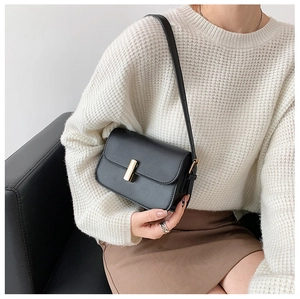 Detail of a minimalist black leather crossbody bag featuring a classic gold metal buckle