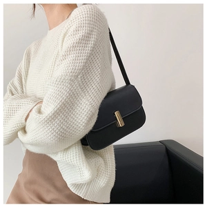 Detail of minimalist black leather crossbody bag featuring a golden rectangular twist lock
