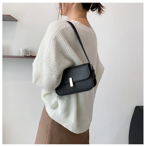 Detail of elegant black leather shoulder bag with gold clasp worn with casual outfit