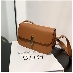 Detail of a brown leather crossbody bag with a gold magnetic clasp on a white book
