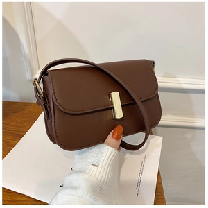 Detail view of small brown crossbody bag with gold metallic buckle on soft white fabric