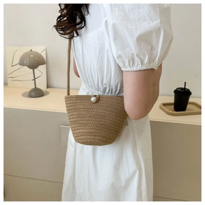 Detail of hand-woven straw crossbody bag featuring an elegant large pearl buckle closure