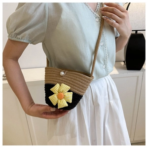 Detail of woven straw bucket bag featuring two-tone contrast and fabric flower with pearl