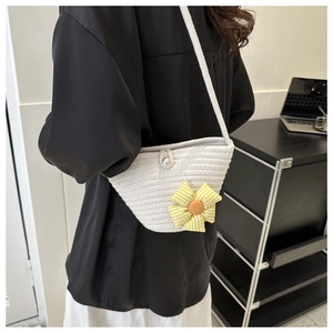 Detail of hand-woven straw crossbody bag featuring a yellow cloth flower and pearl clasp