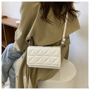 Petit sac bandoulière blanc matelassé sur mannequin avec trench-coat et décor épuré