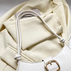 Gros plan d'un sac baguette blanc à motif crocodile avec boucle et bandoulière à nœuds