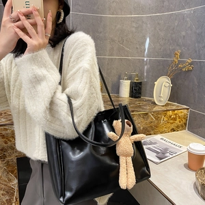 Minimalist black PU leather tote bag with cute bear charm shown on model in modern setting