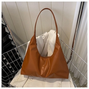 Detail of caramel brown leather hobo bag on white blazer showing soft texture and wide strap