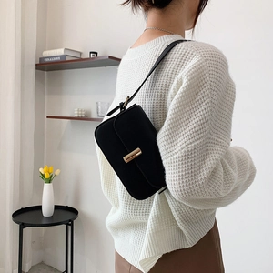 Retro black leather baguette shoulder bag with gold clasp shown on model in home setting