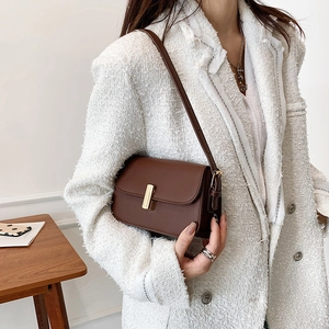 Minimalist brown leather crossbody bag with gold metal buckle shown on a model
