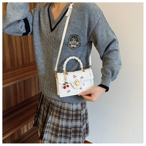 Detail of white crossbody bag featuring cherry print, braided handle, and metal flower buckle