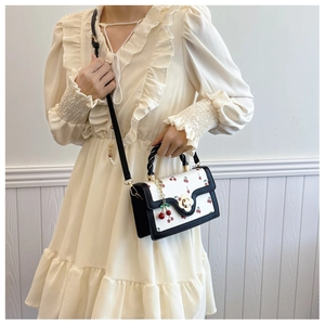 Close-up of white crossbody bag with red cherry prints and golden floral clasp